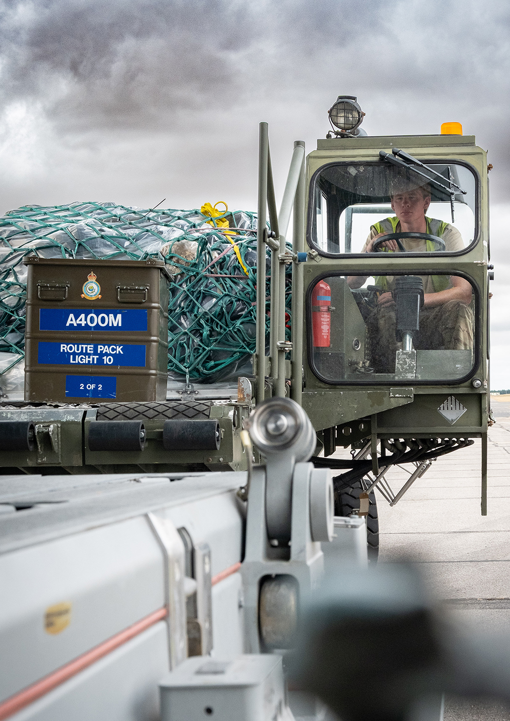 The Condec loader driver operates the vehicle, which is manoeuvring closer to the horizontal ramp of the Atlas (A400M) aircraft. A green military storage container labelled, "A400M ROUTE PACK LIGHT 10", is seen ahead of the loaded pallet.